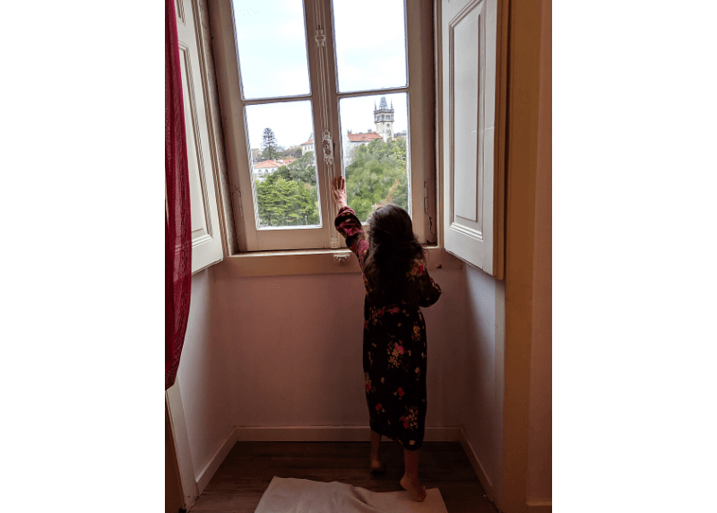 a little girl reaches up on her tip toes to open an old window in an apartment in Sintra Portugal