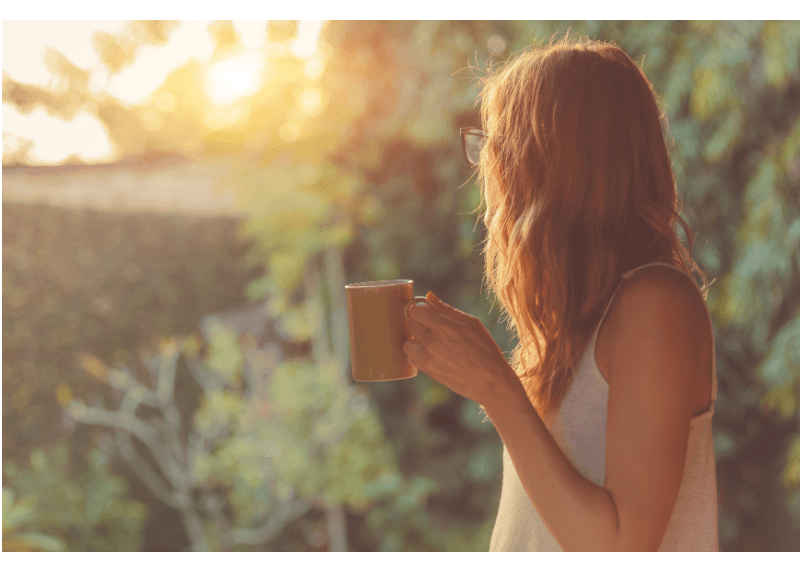 A woman stands outside at sunrise holding a coffee