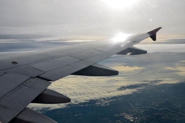 The sun beams off the wing of an airplane in flight.