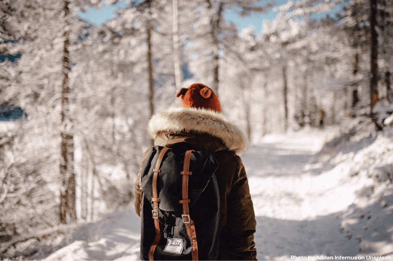 A woman walks through a snowy forest with a little America backpack.