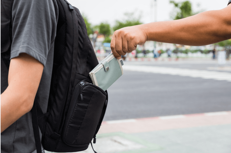 a pickpocket pulls a wallet out of a backpack