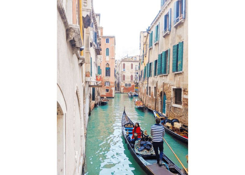 A woman in red floats by in a gondola in Venice.