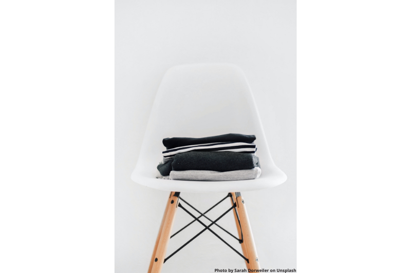 a pile of neutral folded tshirts on a white chair