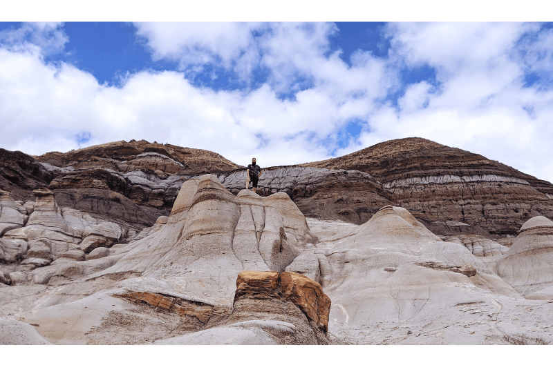 A man stands high above in the white hills of the Drumheller badlands behind the Hoodoos