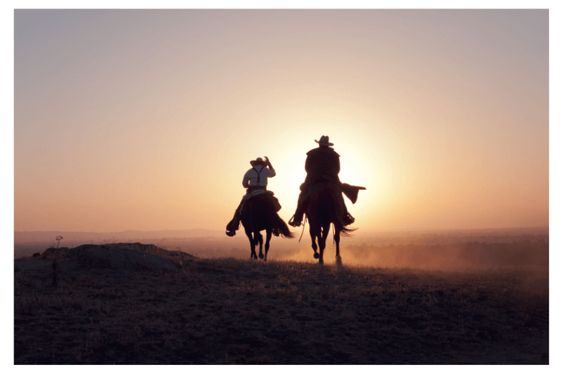 A pair of cowboys riding into the sunset