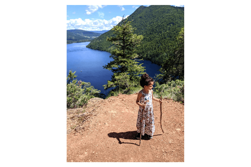 A young girl stands at the top of a steep hike overlooking a lake
