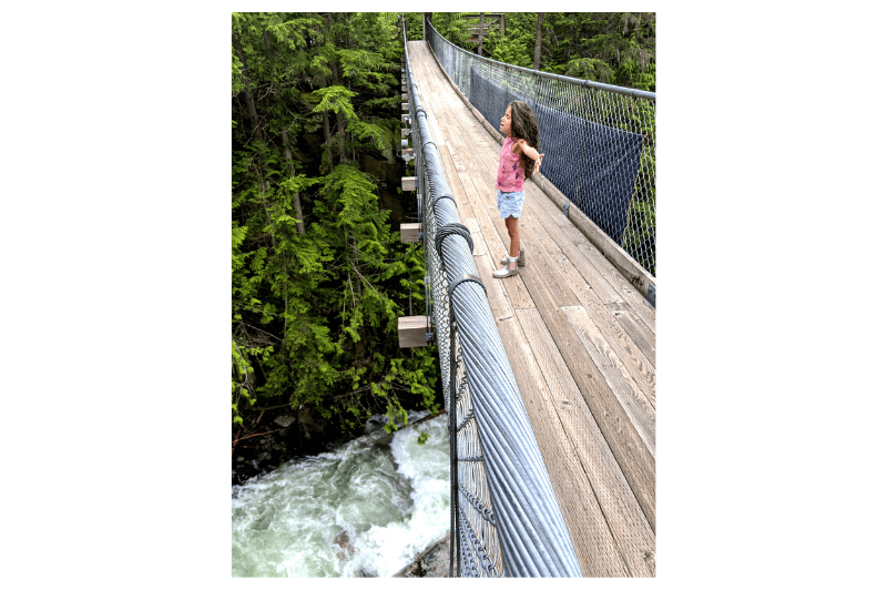 a young girl holds her arms wide on a suspension bridge in Malakwa BC