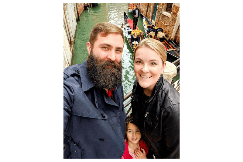 A Mom, Dad, and daughter stand at the edge of a canal in Venice.