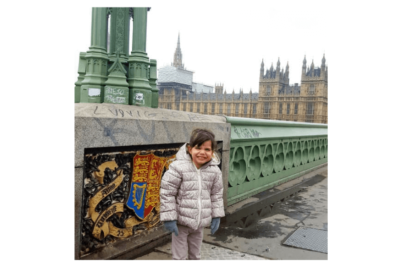 A toddler stands on a bridge near Big Ben