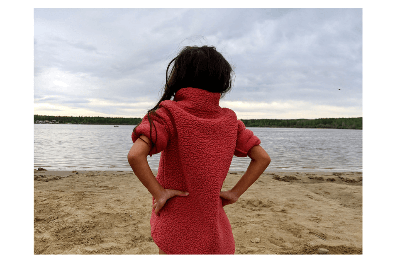A girl stands looking out over a lake with her hands on her hips