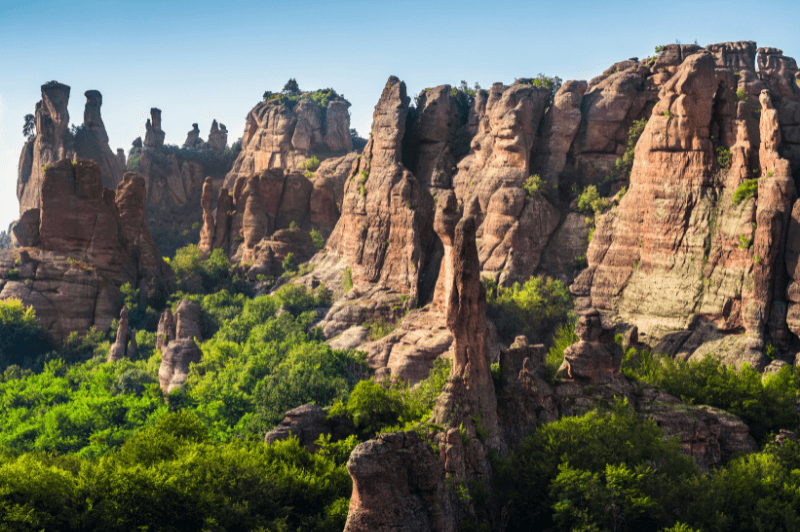 Tall spiky rock formations above green tress at Belogradchik Rocks