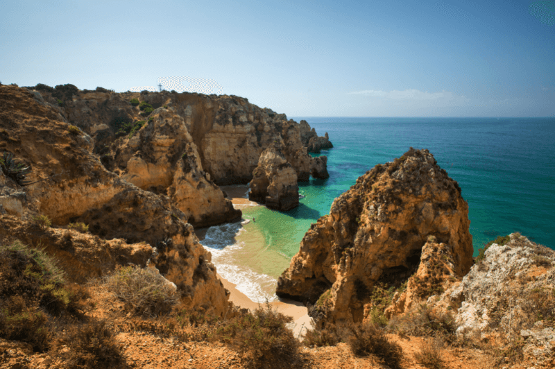 Rocky cliffs hide a sandy beach in between them in a beautiful aquamarine cove near Lagos Portugal