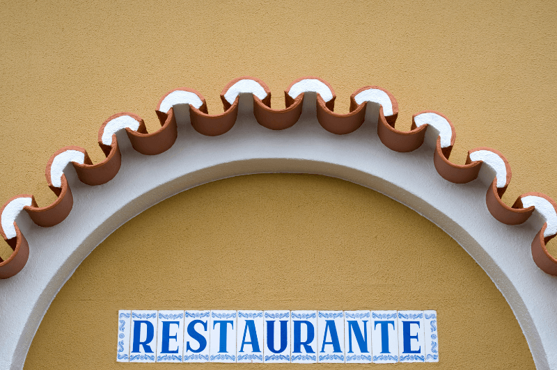 A mustard coloured stucco building in closeup of the arch over the doorway. A blue and white tile sign reads "Restaurante"