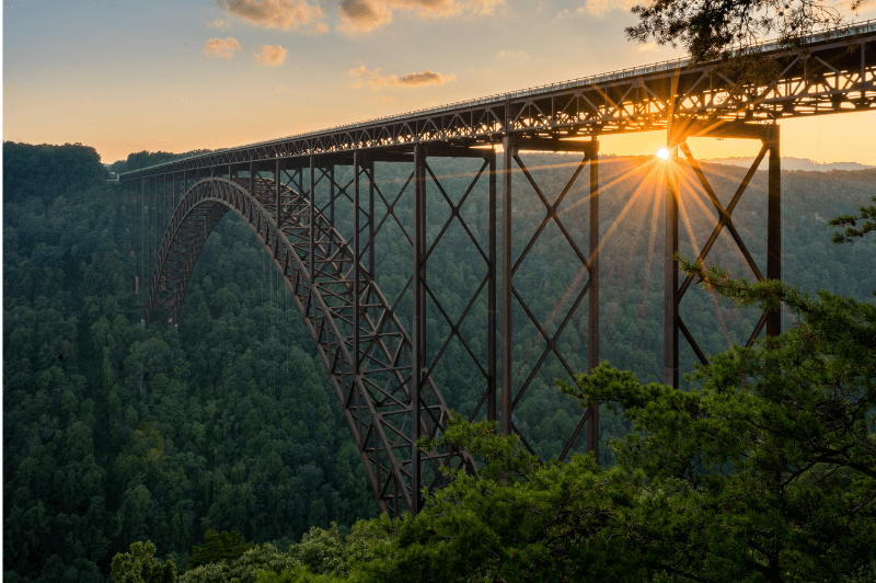 A tall wooden trestle rail bridge in West Virgiia crosses a gorge with the sun setting behind it