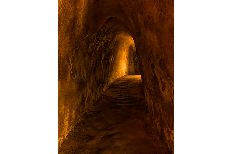 Inside a Cu Chi Tunnel in Vietnam. A simple rounded hallway with a dim orange light at one end