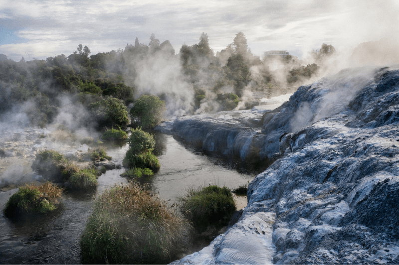 The bubbling geothermal pools of New Zealand's Maori village of Rotorua. A stone ridge sits beside the pools to the right of the frame.