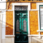 Graphic: A mustard tile fronted home in Portugal with an emerald green door. Text reads "Portugal" at the top and "the perfect slow travel itinerary" at the bottom.