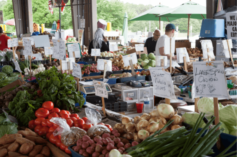 A farmer's market with a multitude of produce on display with handwritten signs in front of it