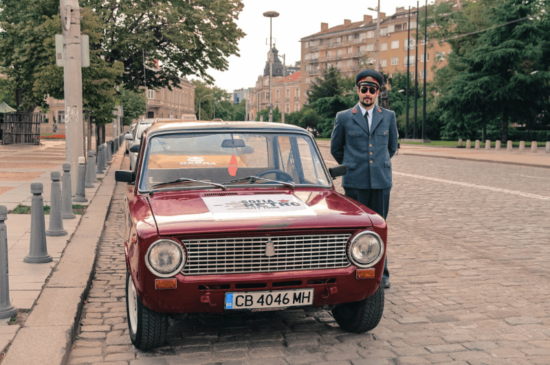 A man in retro suit stands beside a red vintage car in Sofia Bulgaria's city centre