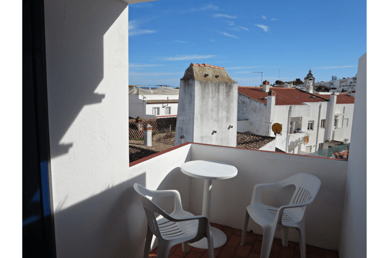 A plastic table and chairs tucked onto a balcony in Lagos Portugal with a view over the city's red rooftops.