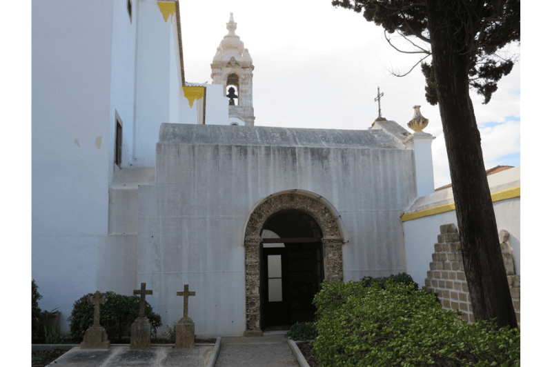 The tiny entrance to the bone chapel in Faro Portugal. An unassuming rounded extension on the back of a whitewashed church.