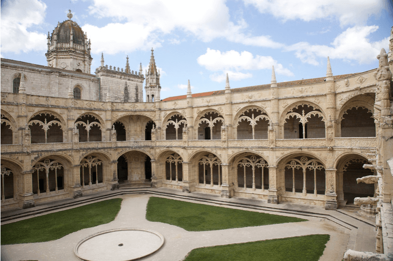 The courtyard at Jeronimos in Lisbon Portugal. The gothic and manueline monastery's archways wrap around an inner courtyard with paths and a fountain in the middle.