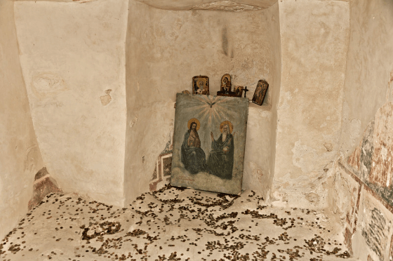 A chapel at Aaladzha Monastery. A shrine is set up against the white wall with a piece of art in front of it. Coins scatter the ground.