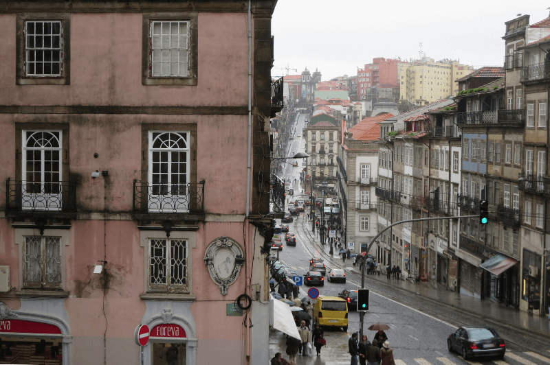 The old town of Porto Portugal. A pink building with dark wooden trim frames the left side foreground of the photo. A street runs alongside the building into the foggy morning. The other side of the street is lined with old Portuguese buildings.