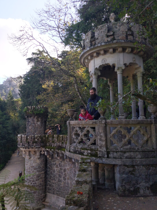 A man stands behind his daughter as they look out from a gothic tower at Quinta da Regaleira called Regaleira Tower