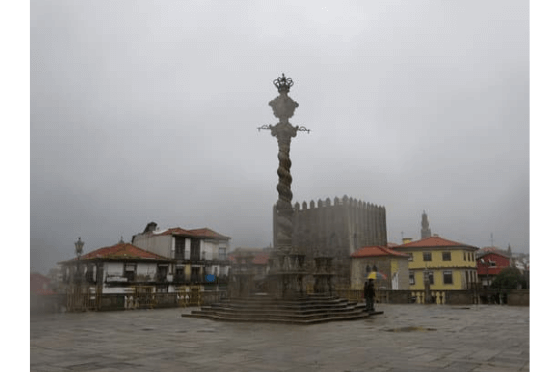 A medieval monument that looks like a wooden scepter outside of the stone building of Porto Portugals tourist information centre