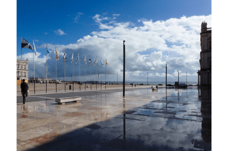 An empty square in Lisbon after the rain. The sky is clearing overhead but puddles have still collected on the ground.