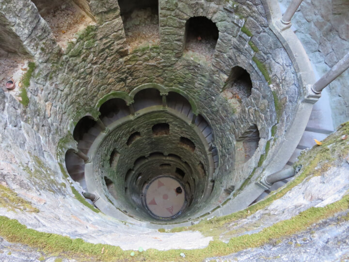 A shot from above on a sunny day into the "subterranean tower" of the Initiation Well at Quinta da Regaleira there is a pink compass at the bottom.