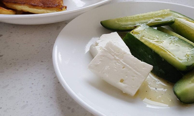 A white plate with cucumber and white bulgarian cheese on it.