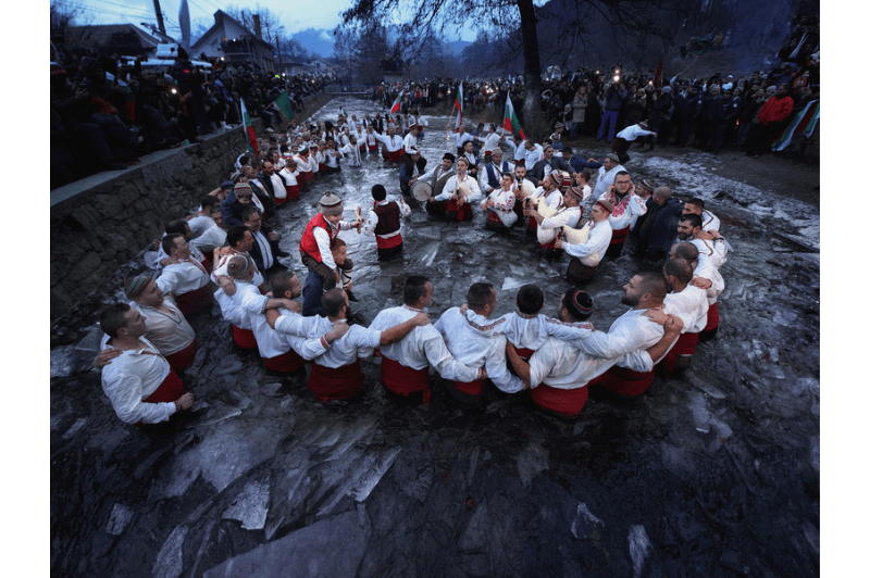 Iordanov Den in Bulgaria. Men in traditional white folk shirts with their arms around each other in the river.