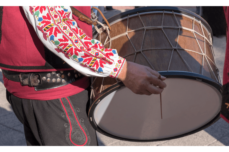 Man in Bulgarian embroidered shirt and pants plays a drum at Iordanov Den