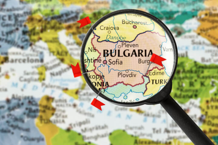 A map of Bulgaria with a magnifying glass over it. Flag pins point out every border where three countries meet.