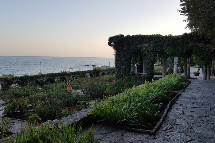 A wine covered gazebo at the end of a black cobbled path at Balchik Palace in the garden overlooking the Black Sea at sunset.