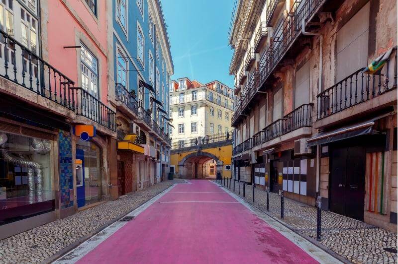 A picture from street level of Rua Nova do Carvalho - Lisbon's pink street - stretching though colorful historic buildings in Lisbon's city center.