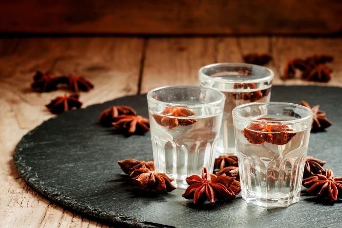 A round placemat on a table with three shot glasses of anise mastika surrounded by scattered anise stars.