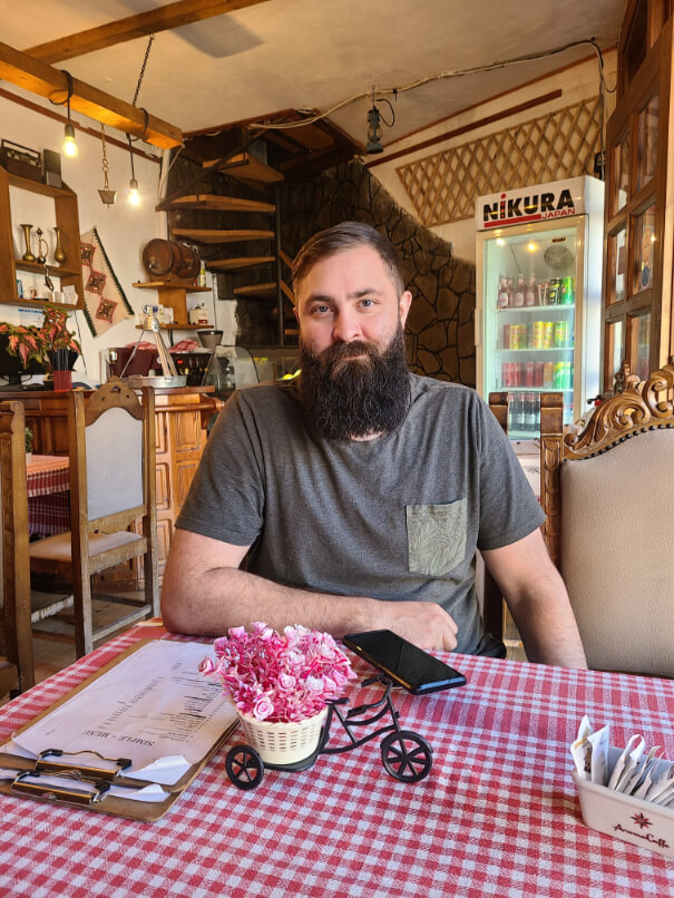 A man with a beard happily enjoying a meal in a cafe in Gjirokastra Albania during a gap year