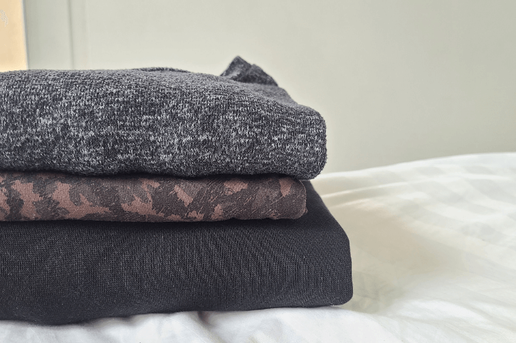 a pile of neutral clothes folded on a bed for packing to travel