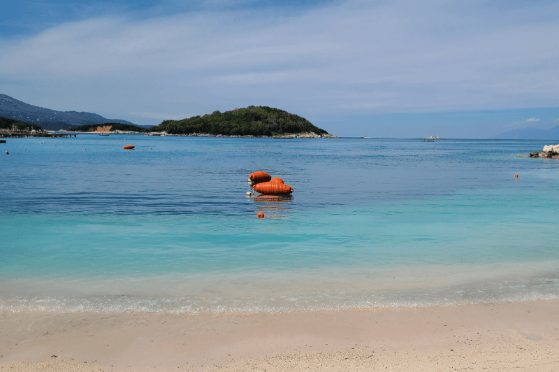 Ksamil Islands in the distance with the sand of Ksamil Beach in the forefront with a beautiful aqua ocean in between