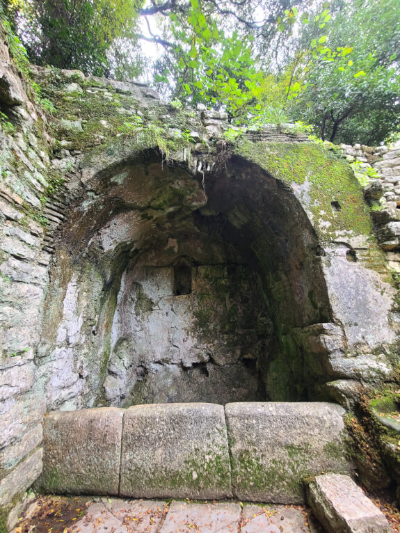 A fountain or well behind the Lion Gate at Butrint National park. A stone archway over a water source. Greek writing is still clear on the front of the well.