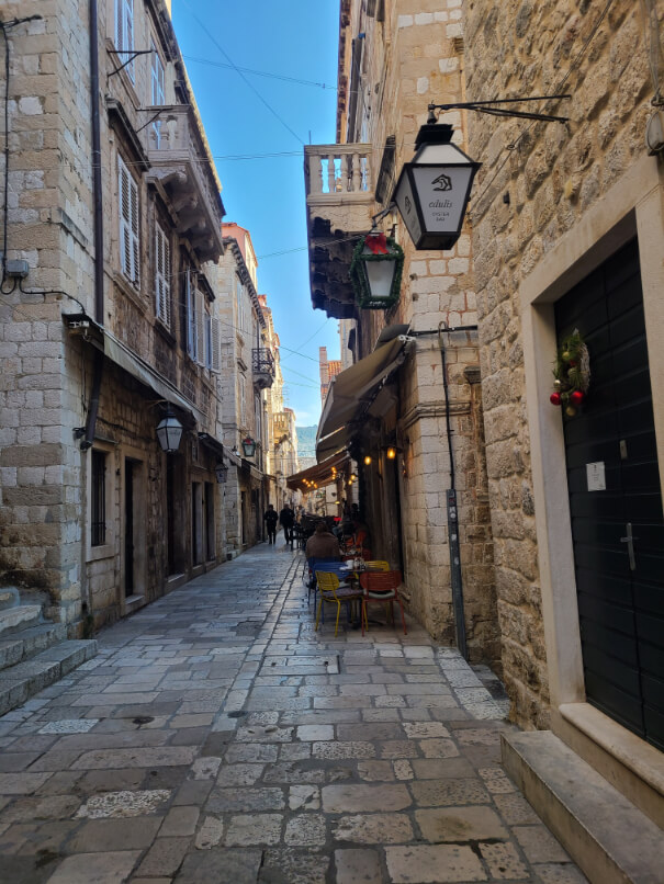 Quiet street in Dubrovnik at Christmas time with a bright blue sky peeking between the buildings above.