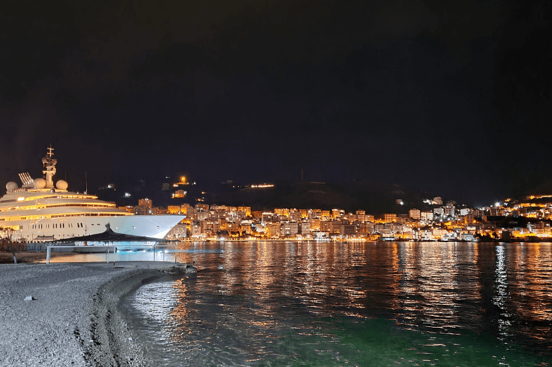 Kodrra Beach with a large yacht in front of Saranda lit up at night