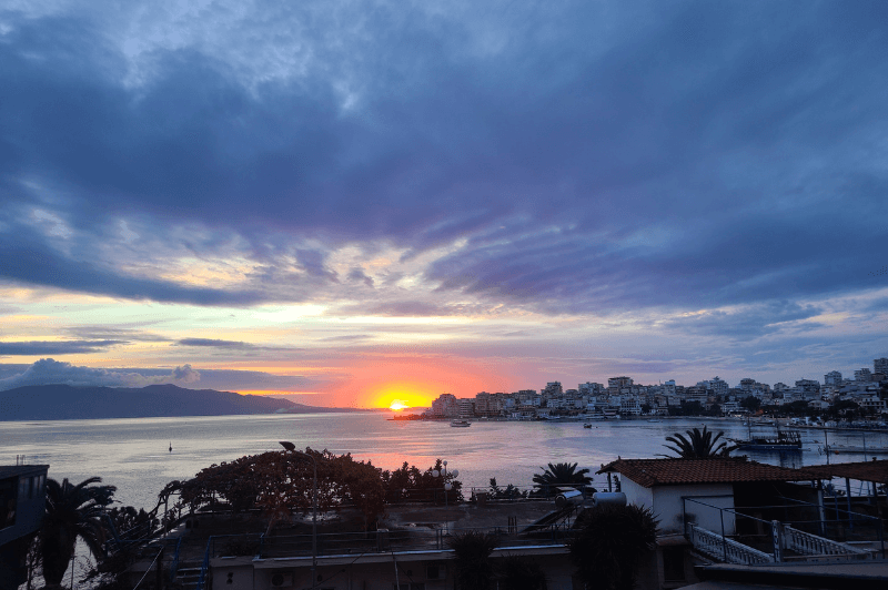 Beautiful sunset in Saranda with a pink, yellow, and orange sun setting in a blue and purple sky.