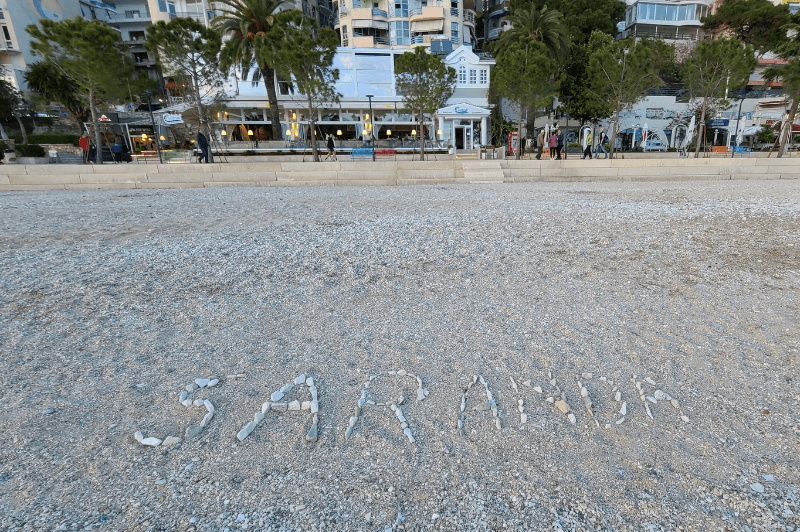 Saranda written in pebbles on Saranda beach with the promenade in the background