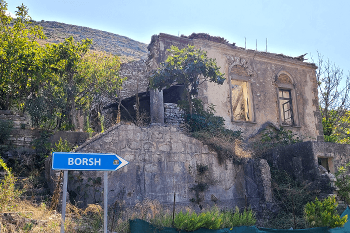 A sign for Borsh below a ruined brick house