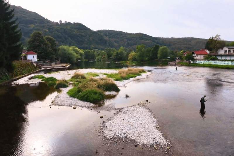 A fisherman in profile on the Una River in Kulen Vakuf with the green mountains behind.